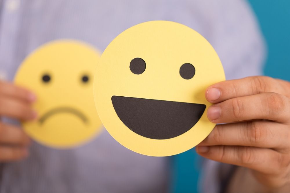 imagem ilustrativa de um emoji sorrindo e por trás um emoji triste para representar a Síndrome de Burnout